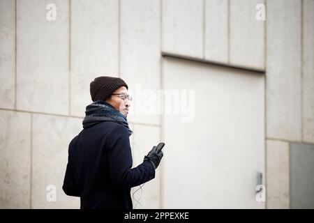 Uomo sorridente che tiene il telefono delle cellule mentre cammina Foto Stock