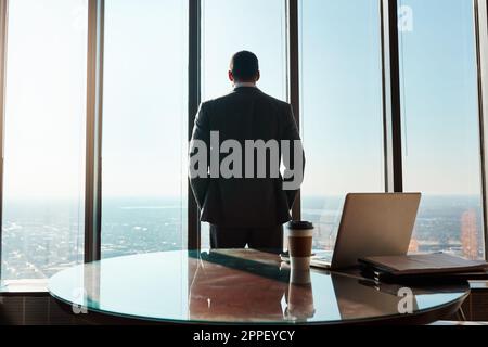 Si è concentrato sul guidare la sua carriera nella giusta direzione. Immagine retroveriva di un giovane uomo d'affari che guarda fuori dalla finestra in un ufficio. Foto Stock