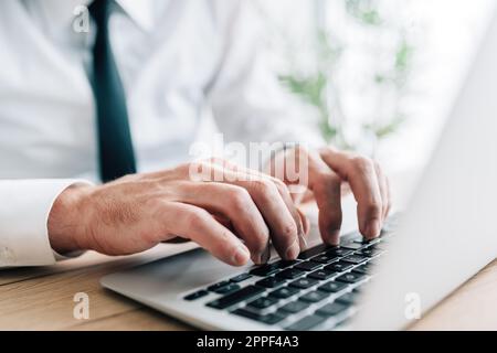 Primo piano ripresa ritagliata di un uomo d'affari bianco colletto utilizzando un computer portatile alla scrivania, tastiera a digitazione mani, messa a fuoco selettiva Foto Stock