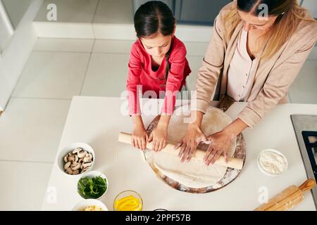 Insegni al vostro bambino le gioie di cottura. Colpo ad angolo alto di una madre di mezza età e di sua figlia che prepara una pizza per andare in forno in cucina a. Foto Stock