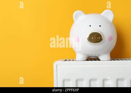 Banco piggy sul radiatore di riscaldamento su sfondo arancione, spazio per il testo Foto Stock