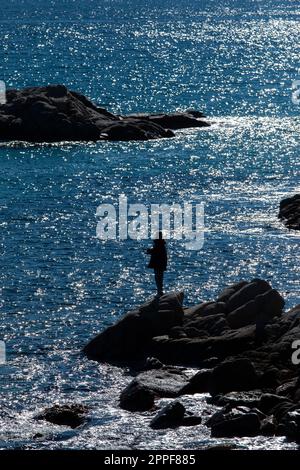 Silhouette di uomo pesca sul mar mediterraneo, in Costa Brava di Spagna, al tramonto. Foto Stock
