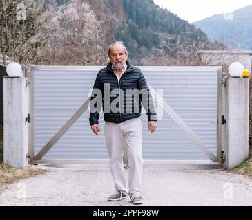 Un uomo che cammina verso il suo cancello automatico, tornando a casa dal lavoro, la sicurezza e la sicurezza della propria casa Foto Stock