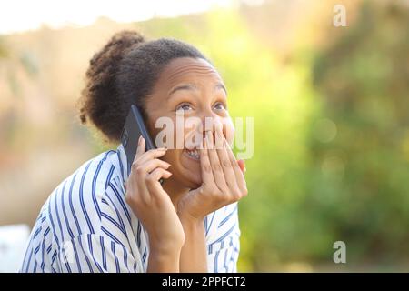 Divertente donna nera che chiama al telefono in un parco Foto Stock