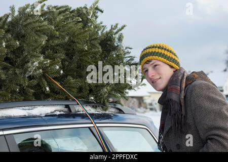Giovane che regge l'albero di natale sul tetto della sua auto, Baviera, Germania Foto Stock