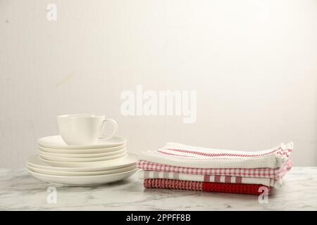 Asciugamani da cucina impilati e stoviglie su un tavolo in marmo bianco, spazio per il testo Foto Stock