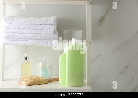 Una pila di asciugamani, spazzola per capelli, shampoo e altri articoli da toeletta su scaffali vicino a pareti di marmo bianco Foto Stock