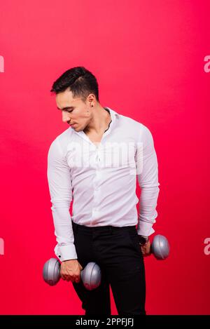 Uomo d'affari con manubri fitness indossare camicia. Riprese da studio su sfondo rosso Foto Stock