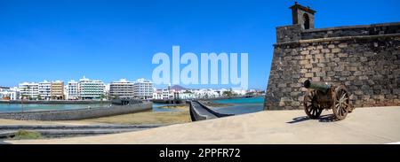 Ammira il cannone di Castillo de San Gabriel con la città di Arrecife sullo sfondo. Foto Stock