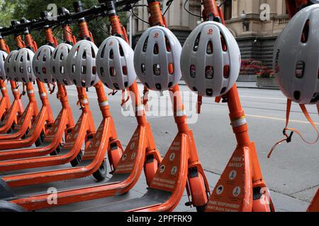 Fila di scooter elettrici condivisi o e-step con caschi in affitto sono in attesa di clienti in una strada a Melbourne, Victoria, Australia. E-mobil Foto Stock