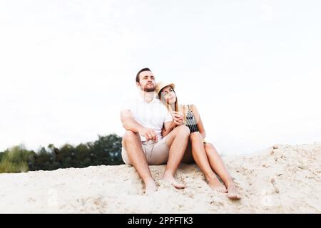 una giovane coppia innamorata è seduta in vacanza su una spiaggia sabbiosa Foto Stock