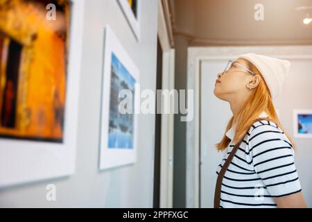 Donna asiatica che guarda una galleria d'arte di fronte a quadri colorati incorniciati Foto Stock