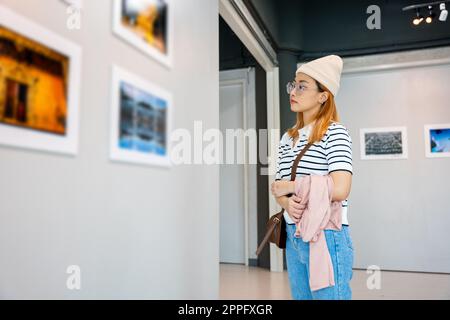 Donna in piedi che guarda una collezione di gallerie d'arte davanti a quadri incorniciati Foto Stock