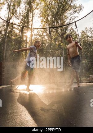 Fratelli al tramonto sul trampolino con acqua spruzzata Foto Stock