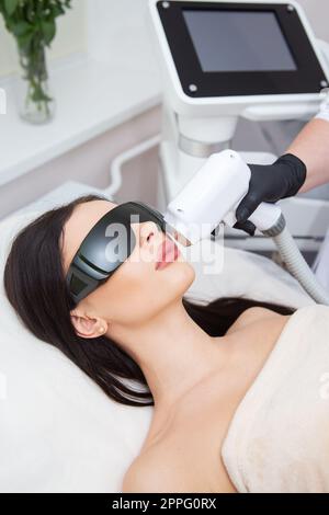 Il processo di depilazione laser del corpo femminile. cosmetologia professionale, epilazione della zona del viso e del labbro superiore. Ragazza con gli occhiali. Concetto di cura del corpo. Foto Stock