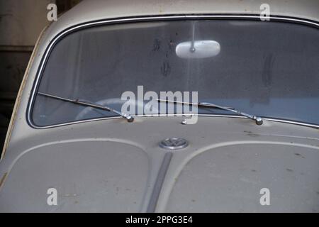 Particolare della parte anteriore di un vecchio scarabeo Volkswagen grigio polveroso con logo, parabrezza, tergicristalli e cofano Foto Stock