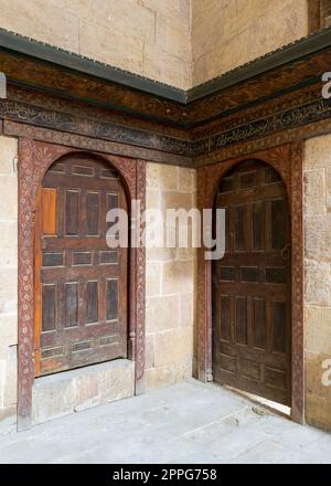 Due porte perpendicolari a volta ornate in legno invecchiate su pareti in mattoni di pietra Foto Stock
