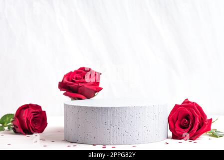Podio vuoto e rose rosse per l'esposizione dei prodotti. Fiori di rosa freschi e piedistallo in cemento, spazio copia. Scena concettuale per prodotti cosmetici, pelle Foto Stock