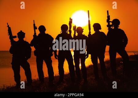 Soldati dell'esercito con fucili arancio silhouette tramonto Foto Stock