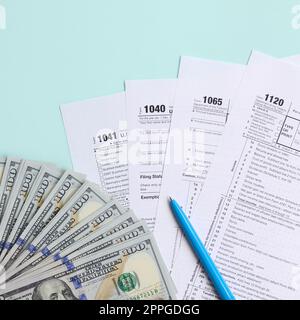 I moduli fiscali si trovano vicino a centinaia di banconote da dollaro e penna blu su sfondo azzurro. Dichiarazione dei redditi Foto Stock