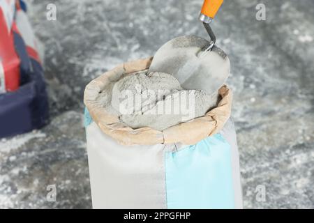 Polvere di cemento e cazzuola messi in borsa su pavimento di pietra, primo piano Foto Stock