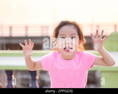 Ragazza giovane cute cheeky, tenendo le mani in su con cinque dita che portano la t shirt rosa, che si attacca verso l'esterno la sua lingua per il volto divertente Foto Stock