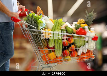 Uomo con carrello pieno di generi alimentari in supermercato, primo piano Foto Stock