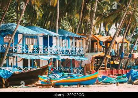 Canacona, Goa, India. Barca da pesca e famose Case ospiti dipinte sulla spiaggia di Palolem sullo sfondo delle palme Tall nel giorno del sole. Foto Stock