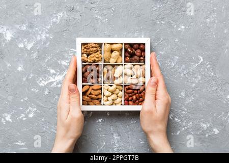 Giovane donna che tiene scatola con noci diverse, primo piano. Primo piano, spazio di copia, vista dall'alto, disposizione piatta. Noce, pistacchi, mandorle, nocciole e anacardi. Foto Stock