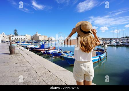 Vacanze in Puglia. Vista sul retro della bellissima ragazza che si gode di una vista sulla città storica di Trani e sul porto. Vacanze estive in Italia. Foto Stock