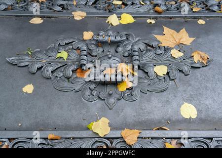 foglie autunnali sul coperchio grigio di una tomba storica ornata in un vecchio cimitero Foto Stock