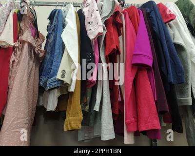 Vestiti appesi agli appendiabiti. Assortimento di articoli di seconda mano. Camicie, bluse, maglioni appesi a un rack per bambini e donne, pronte per la vendita ai clienti. Risparmio di denaro. Belgrado Serbia 22 aprile 2022. Foto Stock