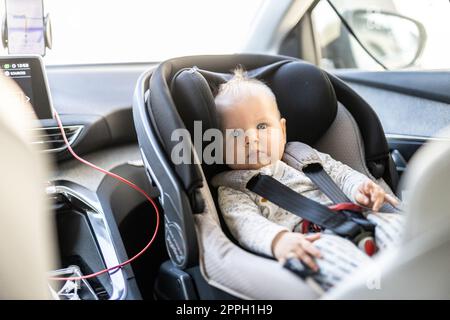 Bambino tenero legato al seggiolino per auto nell'abitacolo durante la guida dell'auto. Foto Stock