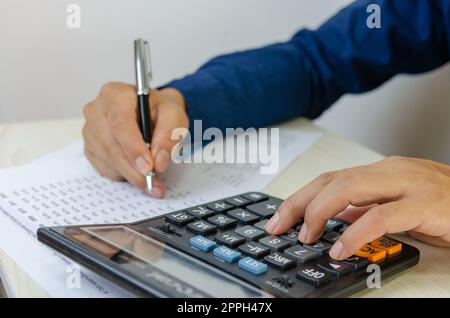 Mano che usa la calcolatrice e la scrittura faccia il contabile di nota che lavora sulla statistica di vendita di rapporto di finanza di affari in ufficio. Foto Stock
