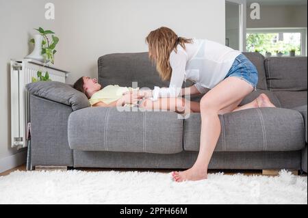 Madre amorevole solletico sua figlia sul divano a casa Foto Stock