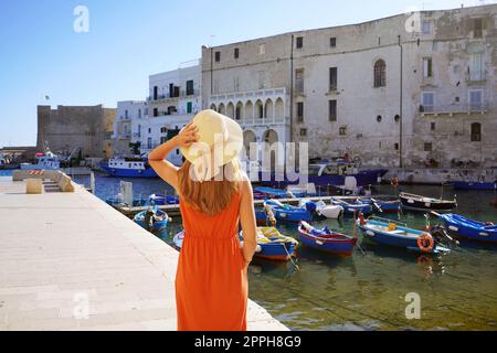 Vacanze in Puglia. Vista posteriore di una bella ragazza alla moda che gode di una vista sull'antico porto di Monopoli in Puglia. Vacanze estive in Europa. Foto Stock