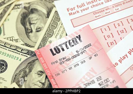 Il biglietto della lotteria rossa si trova su fogli da gioco rosa con numeri da segnare su banconote da cento dollari. Concetto di gioco alla lotteria o dipendenza dal gioco d'azzardo. Primo piano Foto Stock