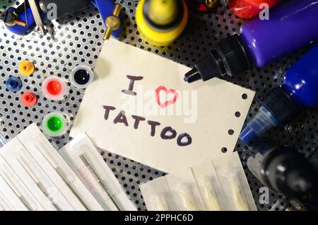 Amo il tatuaggio. Il testo è scritto su un piccolo foglio di carta tra varie attrezzature per il tatuaggio Foto Stock