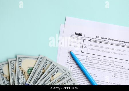 il modulo fiscale 1065 si trova vicino a cento banconote da dollaro e penna blu su sfondo azzurro. GLI STATI UNITI ritornano per il reddito della famiglia Foto Stock