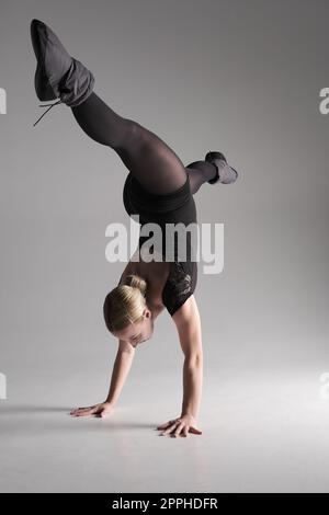 Balletto donna danzatrice vestito nero su sfondo grigio, Ballerina posa e mostra la sua flessibilità su sfondo grigio in studio Foto Stock