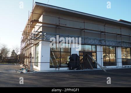 Impalcature su una nuova casa a un piano. La facciata funziona. Creazione di affari. Basso edificio privato. Intonacare il muro di un edificio. Edificio di negozi. Strutture per la produzione di metalli. Foto Stock