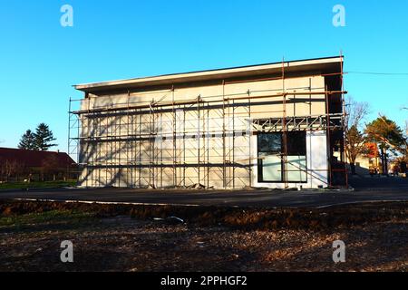 Impalcature su una nuova casa a un piano. La facciata funziona. Creazione di affari. Basso edificio privato. Intonacare il muro di un edificio. Edificio di negozi. Strutture per la produzione di metalli. Foto Stock