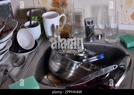 Un enorme mucchio di piatti non lavati nel lavandino della cucina e sul ripiano Foto Stock