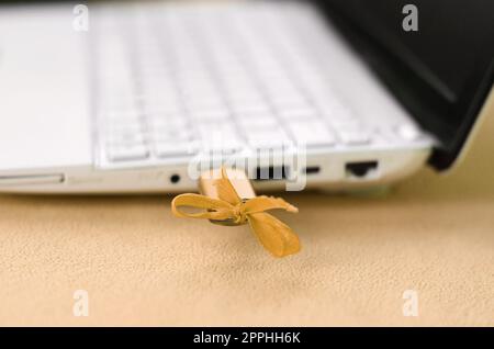 Un'unità flash USB arancione con fiocco è collegata a un computer portatile bianco, che si trova su una coperta di morbido e soffice tessuto in pile arancione chiaro. Design femminile classico per una scheda di memoria Foto Stock