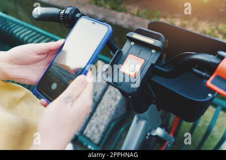 Donna prende una bicicletta noleggiata in un parcheggio con smartphone Foto Stock