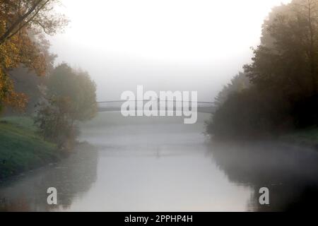 Solitario ciclista al mattino o alla sera nebbia sul ponte sul piccolo fiume Foto Stock