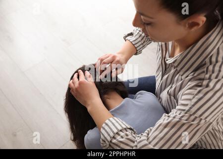 Madre che esamina i capelli di sua figlia in casa. Trattamento antighiaccio Foto Stock