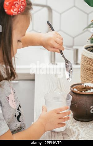 La piccola ragazza dai capelli scuri di 3 anni con la fascia prepara la torta di mele in cucina. Il bambino mette la farina nel dosatore. Verticale Foto Stock