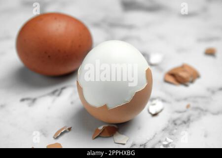 Uova bollite e pezzi di guscio su tavola di marmo bianco, primo piano Foto Stock