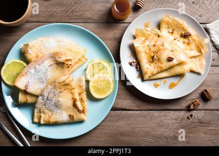Crepes con vari condimenti - miele e noci pecan, agrumi di limone su sfondo di legno. Crepes fatti in casa per colazione o dessert. Foto Stock